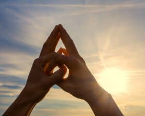 Hands forming a mudra against the backdrop of a bright sun and a clear sky, symbolizing meditation and energy at The MataJi Sanctuary.