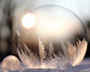 Close-up of two frozen soap bubbles with delicate ice crystal patterns, glistening in sunlight against a blurred, soft-focus background.