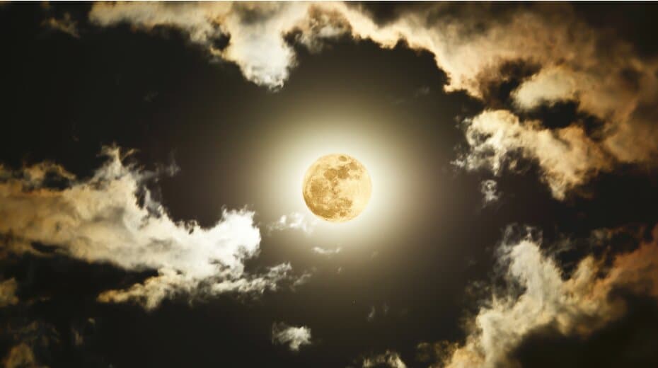 Full moon surrounded by clouds in a night sky, radiating a soft glow.