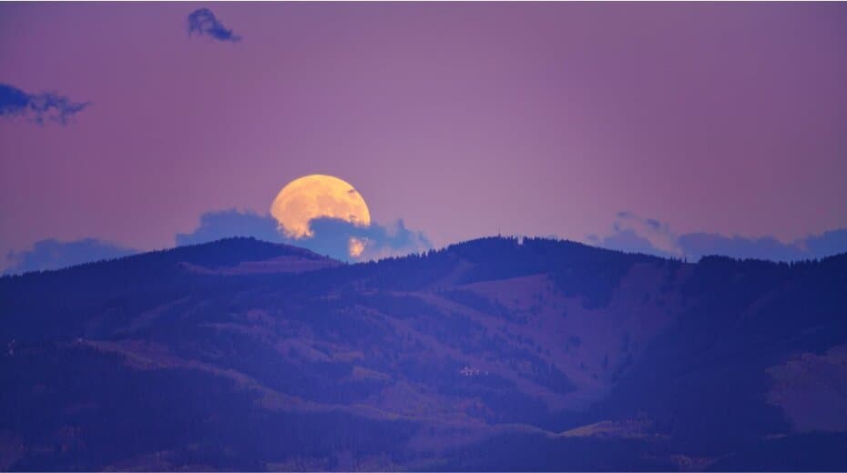 Full moon rising over dark, rolling hills under a purple sky, evoking a serene and meditative atmosphere.