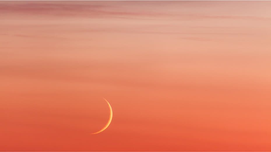 Crescent moon against a peach and pink sky at sunset.