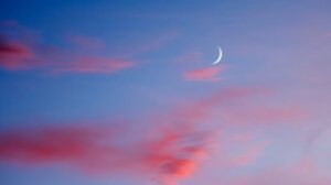 Crescent moon and pink clouds in a serene blue sky, evoking tranquility and meditation.