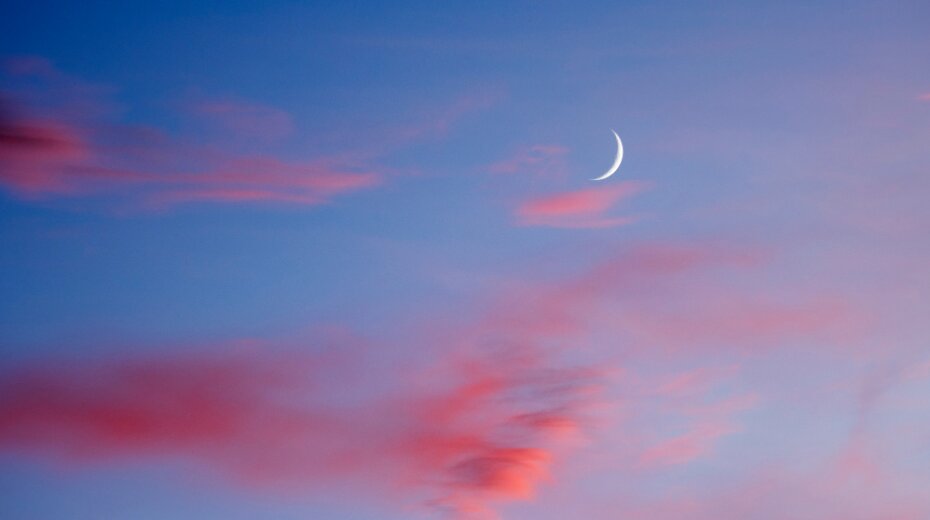 Crescent moon and pink clouds in a serene blue sky, evoking tranquility and meditation.