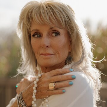 Portrait of a woman with long blonde hair, wearing jewelry, gazing thoughtfully outdoors, embodying serenity and wisdom.