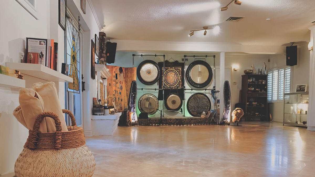 Spacious yoga studio featuring a wall of gongs, soft seating, and a warm, inviting atmosphere for meditation and wellness events.